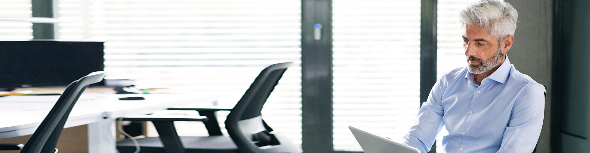 Mas seguros para empresas - Hombre de negocios con camisa y gafas de mediana edad sentado en una silla en la oficina buscando seguros para empresas en una tablet Mas seguros para empresas - Hombre de negocios con camisa y gafas de mediana edad sentado en una silla en la oficina buscando seguros para empresas en una tablet