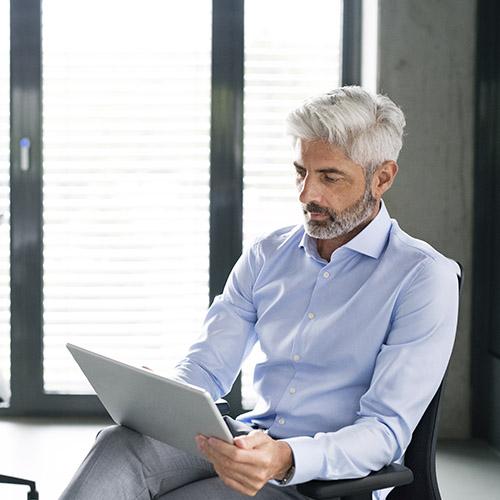 Más Seguros para Empresas - Hombre de negocios de mediana edad sentado en una silla en la oficina con una tablet